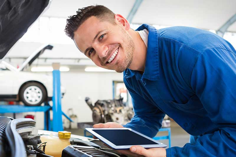 A GMC Maintenance Professional smiles at the camera while servicing an SUV engine